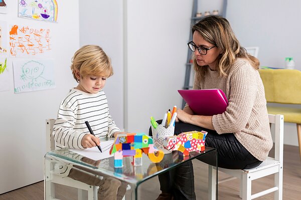 Enfant qui dessine et femme représentant une psychologue pour enfant