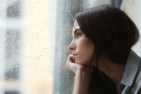 Jeune femme qui regarde par la fenêtre alors que la pluie tombe. Cette photo représente la tristesse qui peut amener à consulter un psychologue pour adultes à Barcelone